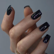 Nail polish bottle with 'Luna' branding and a black glittery nail sample on a pink background