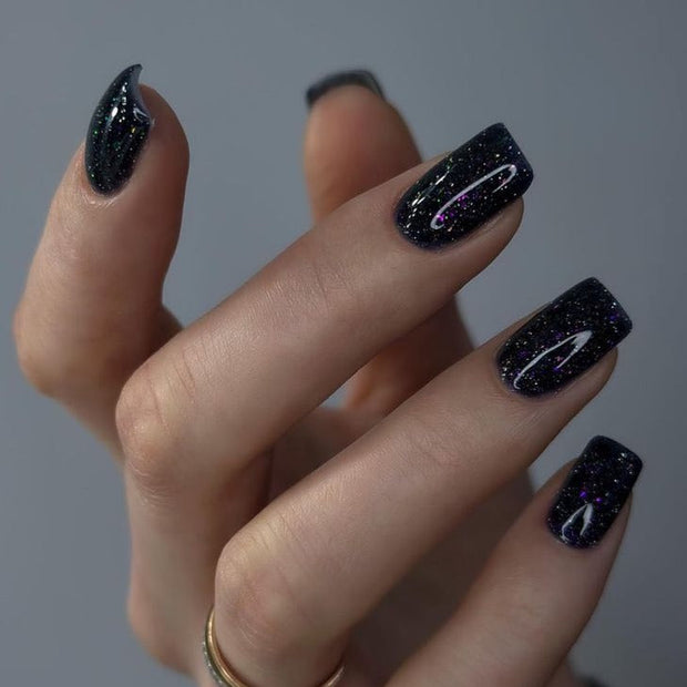 Nail polish bottle with 'Luna' branding and a black glittery nail sample on a pink background
